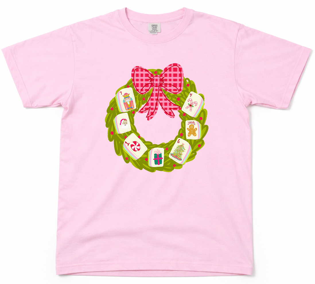 Pink t-shirt with a Christmas wreath design featuring a bow and small images on a white background.