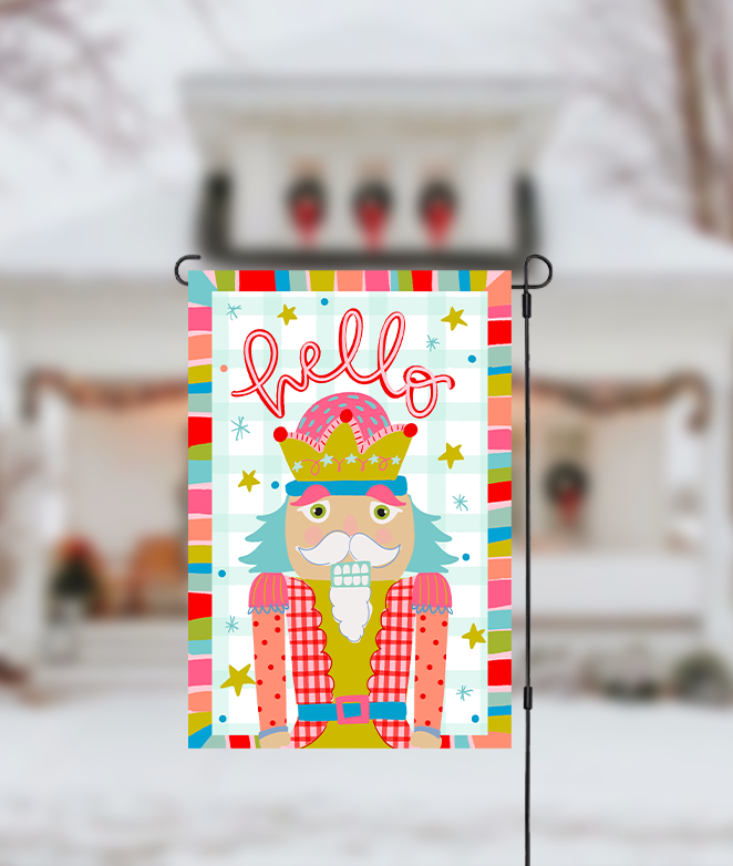 Decorative garden flag with a colorful design featuring a nutcracker and the word 'Hello' on a blurred background.