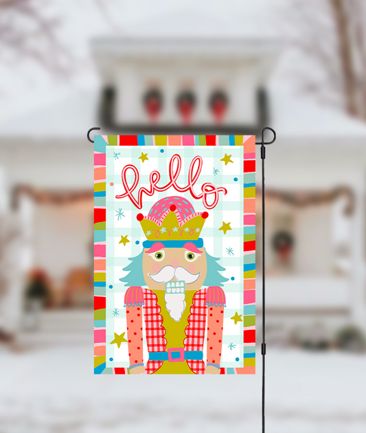 Decorative garden flag with a colorful design featuring a nutcracker and the word 'Hello' on a blurred background.