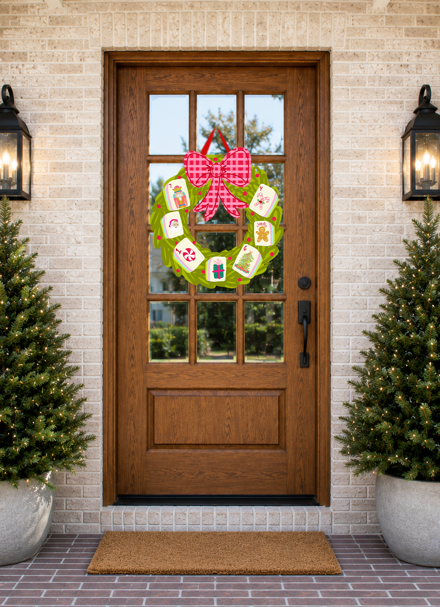Wooden front door with a decorative wreath featuring cards and a pink bow, flanked by two potted trees on a brick patio.