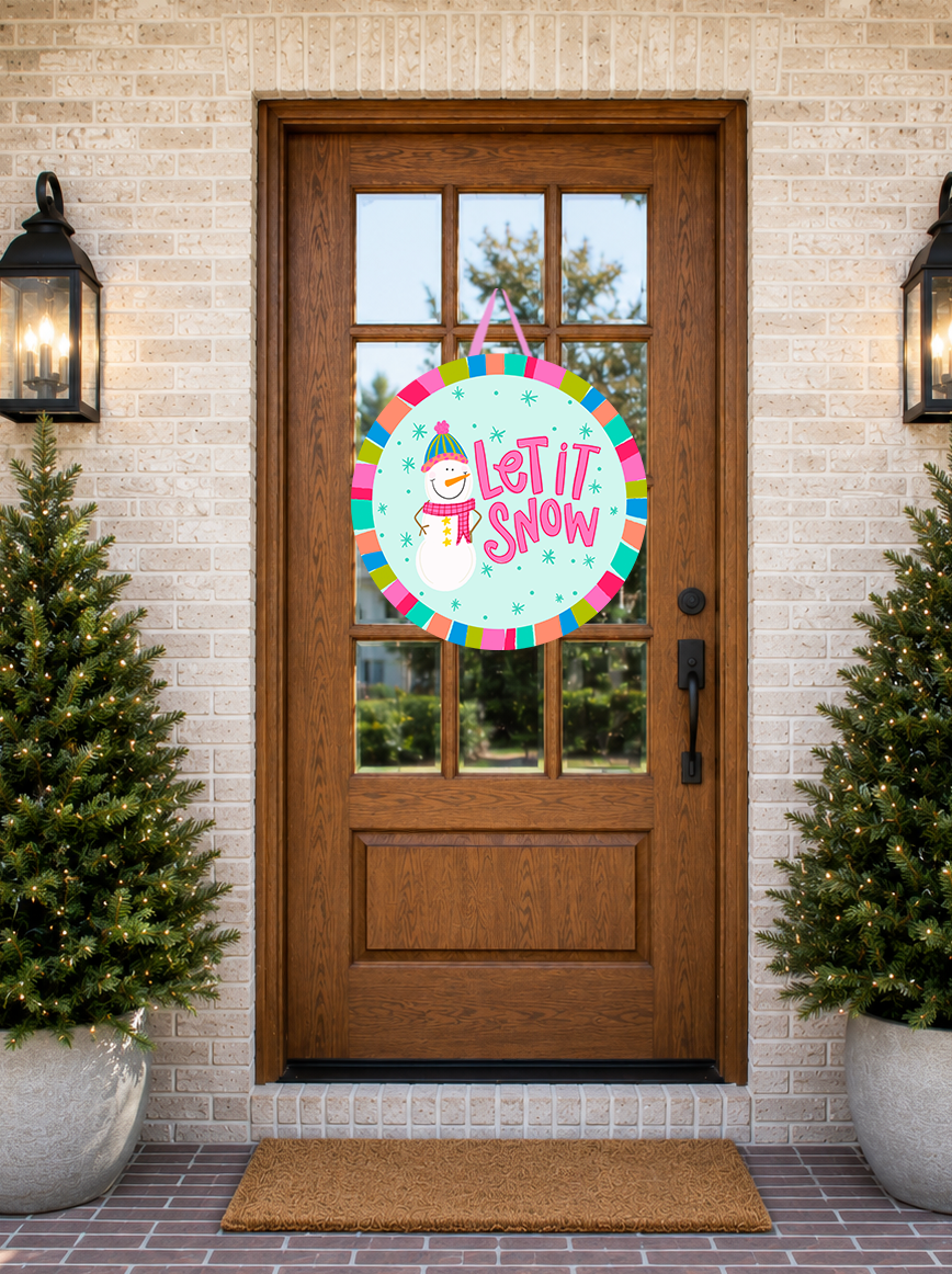 Decorative 'Let It Snow' sign hanging on a wooden door with Christmas trees and lights.