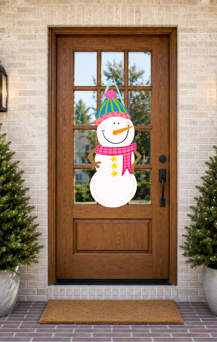 Decorative snowman door hanger on a wooden front door with Christmas trees and a doormat.