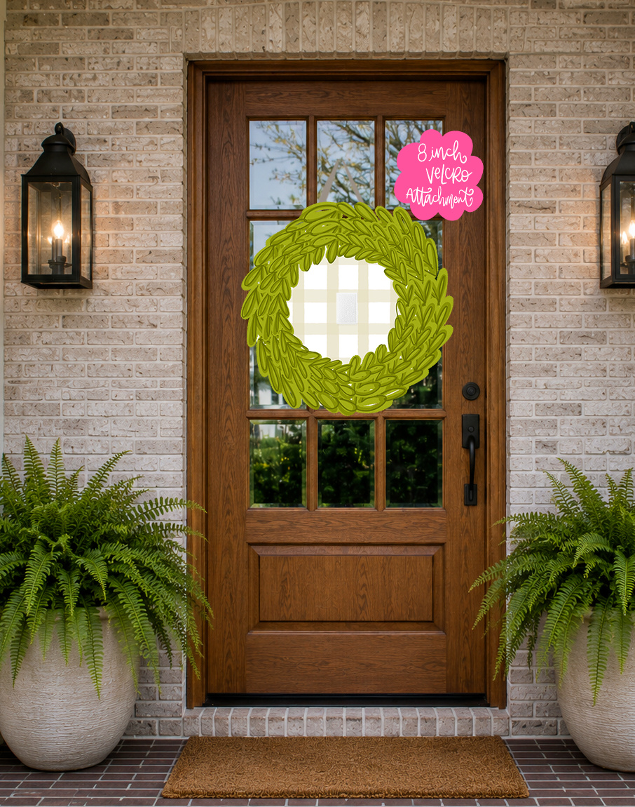 Wooden front door with a green wreath and a pink sign on a brick wall.