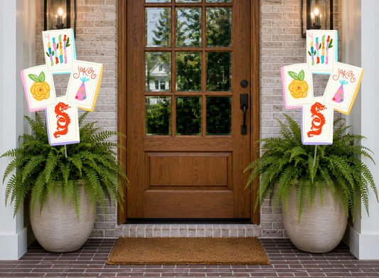 Decorative signs with colorful designs on a door with potted plants on either side.
