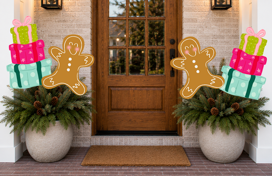 Decorative gingerbread men and gift boxes on potted plants in front of a door.