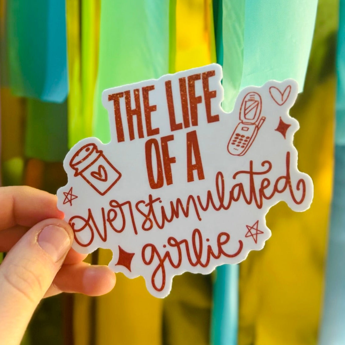 Doodles by Rebekah "The Life of an Overstimulated Girlie" sticker. This humorous hand-painted vinyl decal features coffee and flip phone icons, making it a perfect relatable gift for friends to use on water bottles, laptops, and planners.
